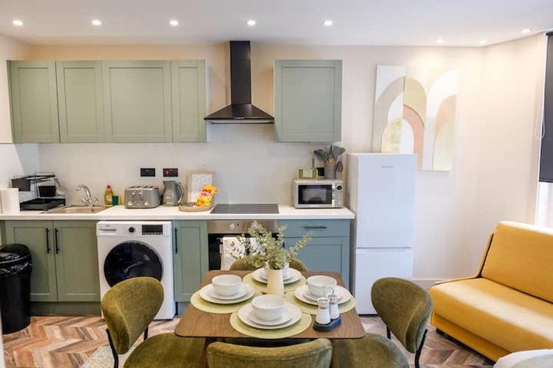 Modern kitchen-diner with sage green cabinetry, dining table set for four, and yellow accent seating