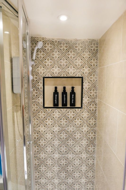 Bathroom shower area with geometric tile wall and three dark bottles in wall niche