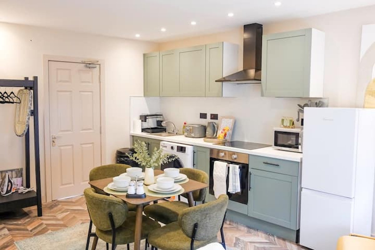 Modern kitchen with sage cabinetry, dining table, and integrated appliances