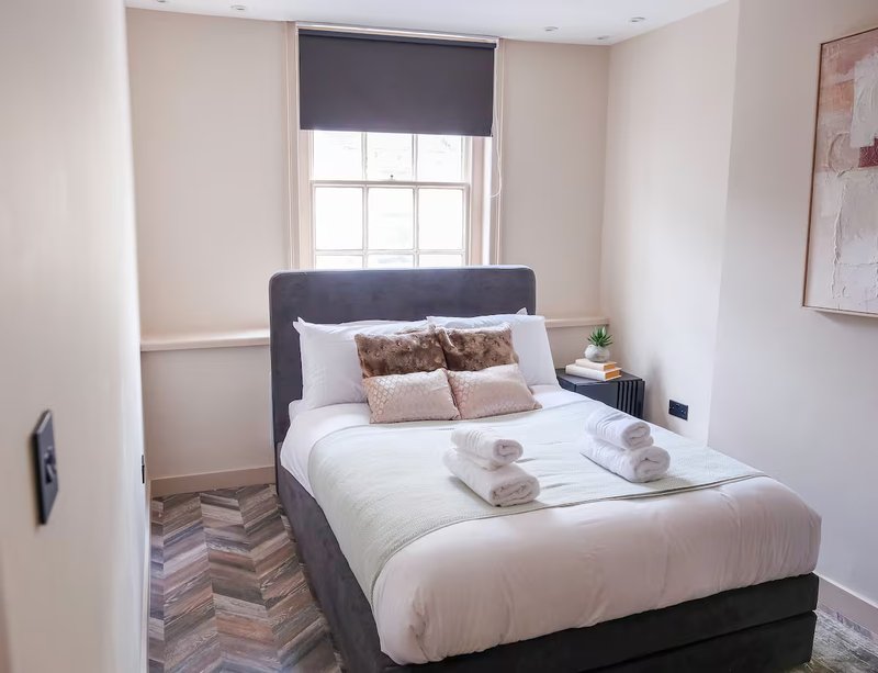 Bedroom with double bed, dark headboard, white bedding, decorative pillows and rolled towels
