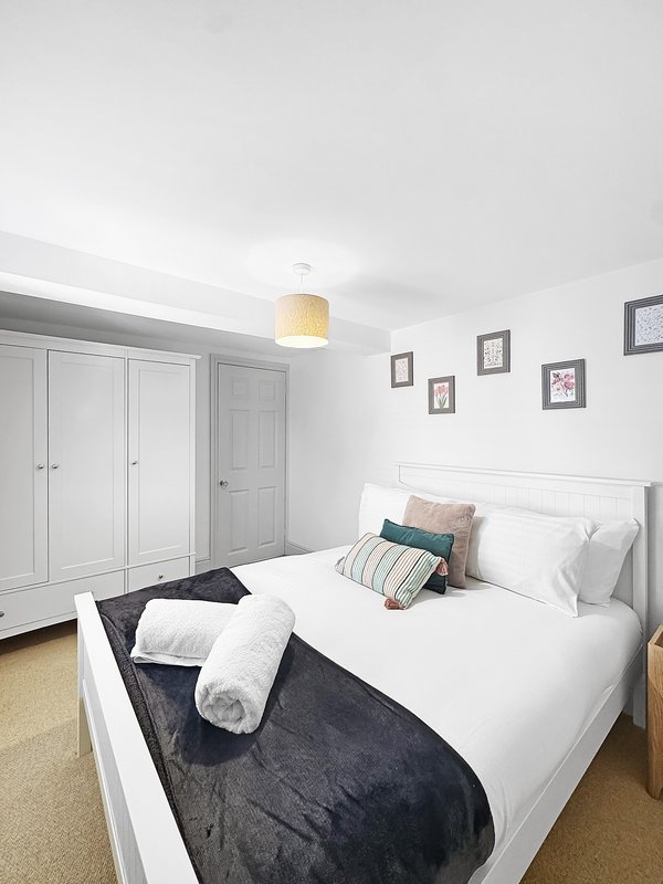 Bright bedroom with double bed, white wardrobe, pendant light, and framed wall art