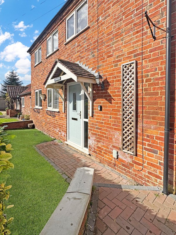 Brick semi-detached house exterior with white door, windows, and manicured front garden