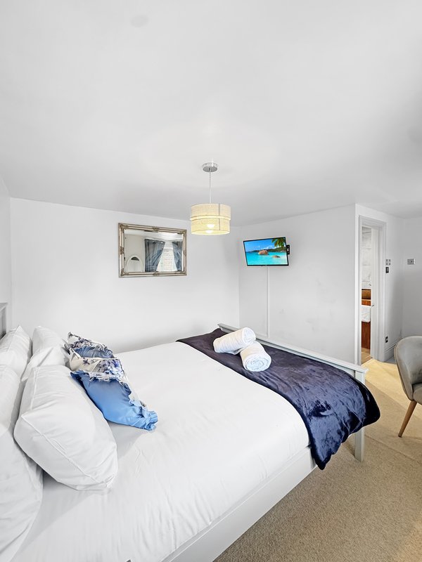 Bright bedroom with double bed, white bedding, blue cushions, wall-mounted TV and pendant light