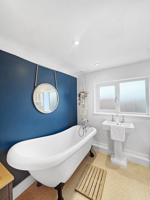 Modern bathroom with freestanding white bathtub, pedestal sink, round mirror and blue accent wall