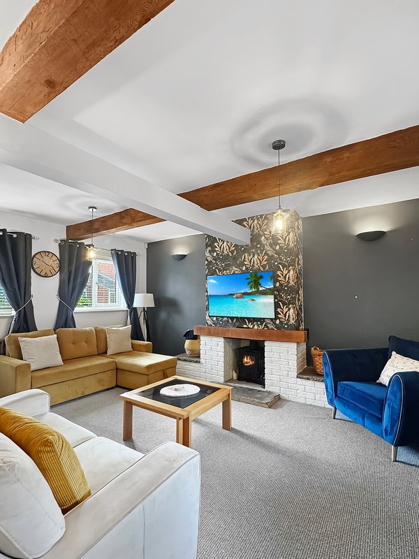 Modern living room with exposed wooden beams, fireplace, TV, and mixed seating