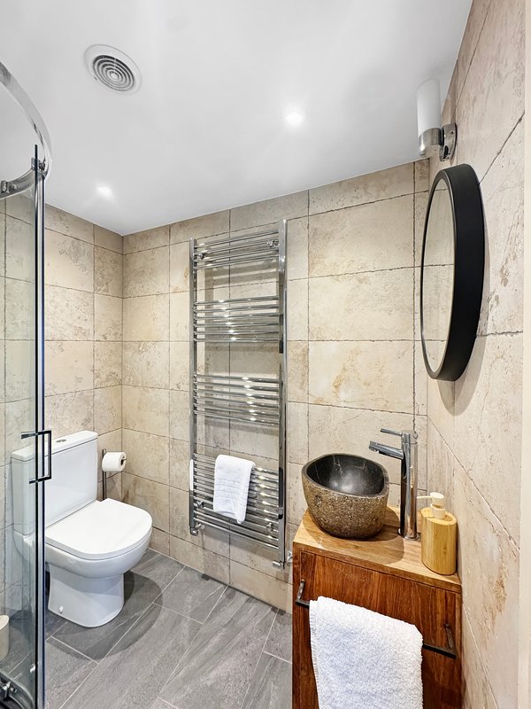 Modern bathroom with toilet, heated towel rail, walk-in shower, and wooden vanity with vessel sink