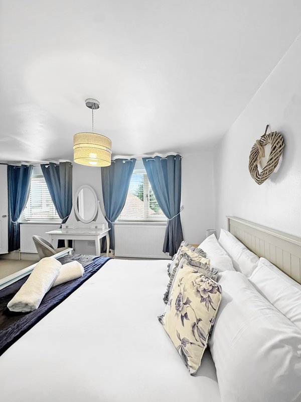 Bright bedroom with double bed, blue curtains, pendant light, and coastal decor