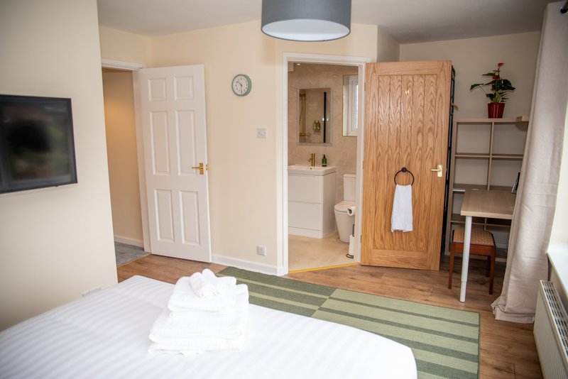 Bedroom with double bed, ensuite bathroom, wooden floors, and storage shelving