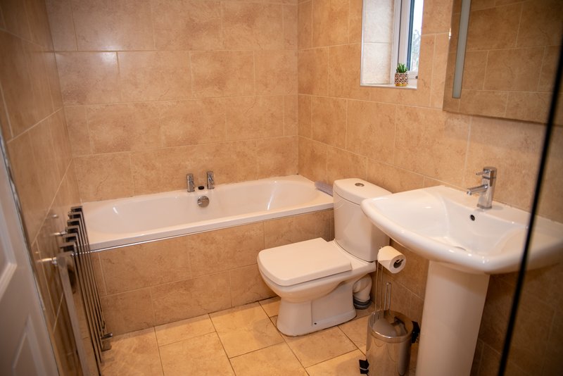 Bathroom with bathtub, toilet, pedestal sink, towel rail and terracotta tiles