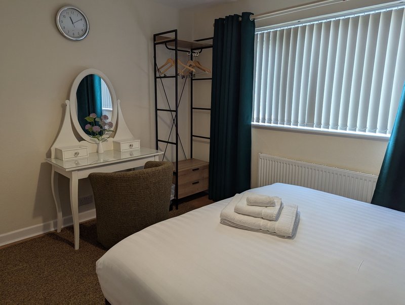 Bedroom with double bed, white dressing table, mirror, chair and window with vertical blinds