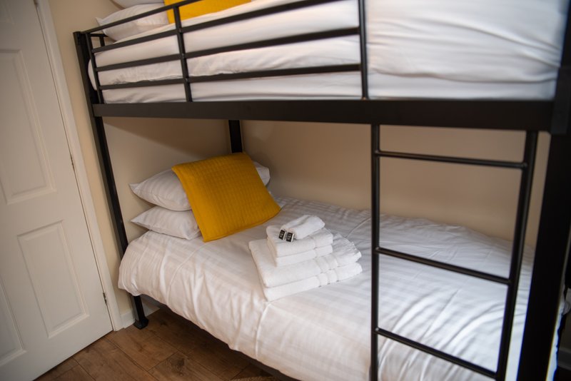 Bunk bed with black metal frame, white bedding, yellow cushion and folded towels