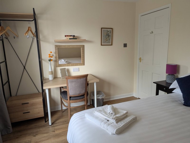 Bedroom with double bed, wooden desk, chair, shelving unit and white wardrobe door