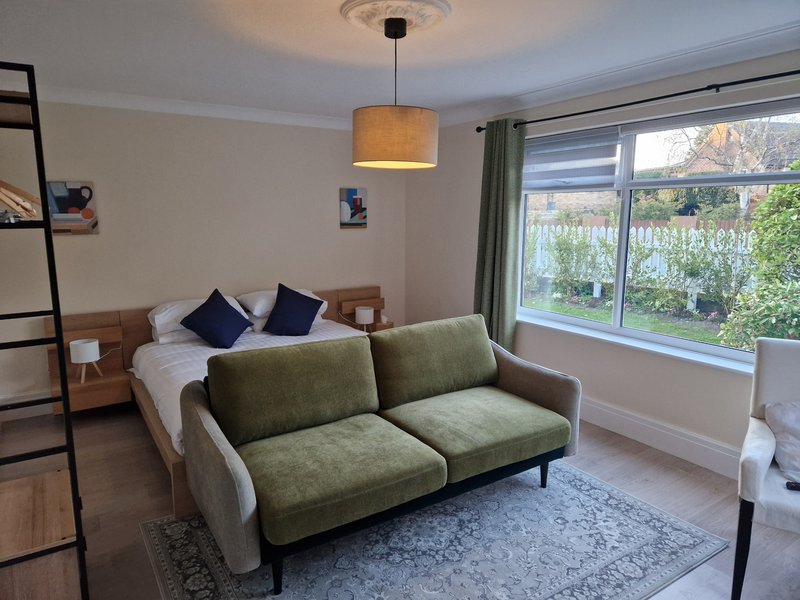 Studio bedroom with double bed, green sofa, pendant lamp and garden views