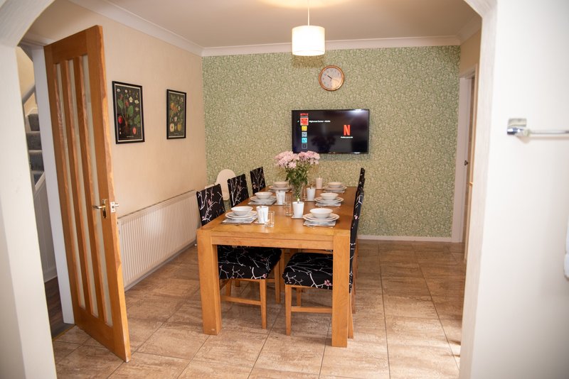 Dining room with wooden table, black chairs, green wallpaper and wall-mounted TV