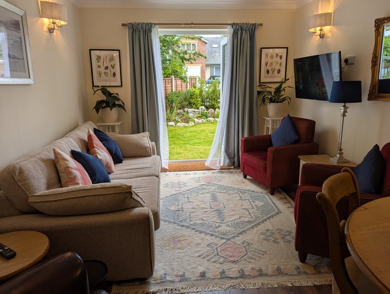 Bright living room with cream sofa, red armchair, TV, and open doors to garden