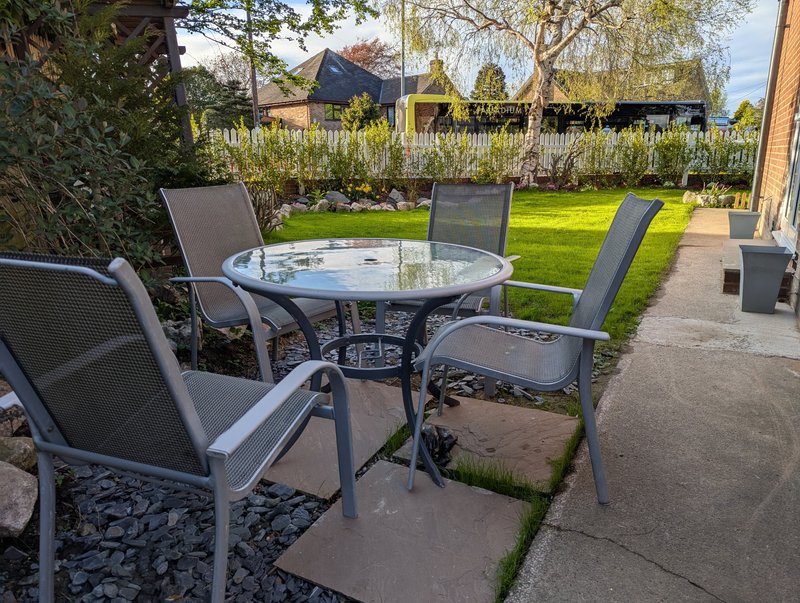 Patio seating area with round table, four chairs, garden and lawn beyond