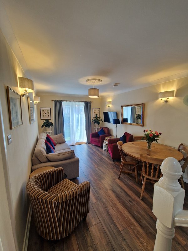 Open-plan living and dining area with striped armchairs, sofa, dining table, and glass balcony doors