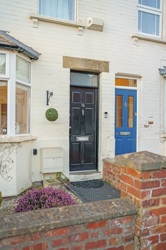 Terraced house exterior with black front door, blue door, cream and white facade, brick wall and purple flowering plants