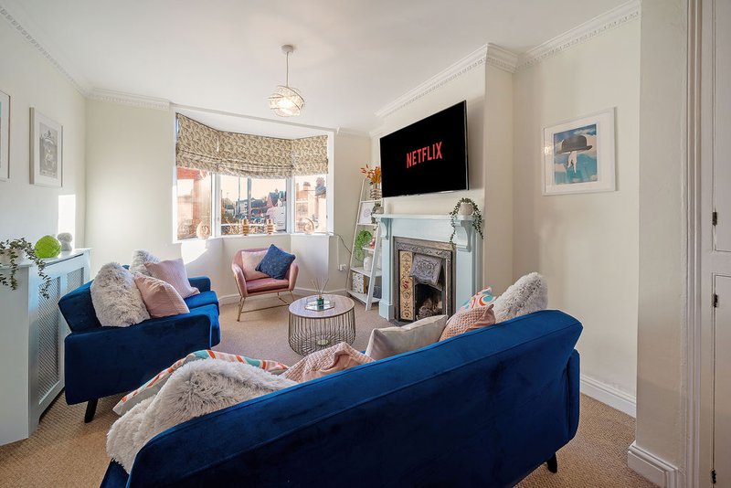 Bright living room with blue sofas, fireplace, mounted TV, and bay window seating area
