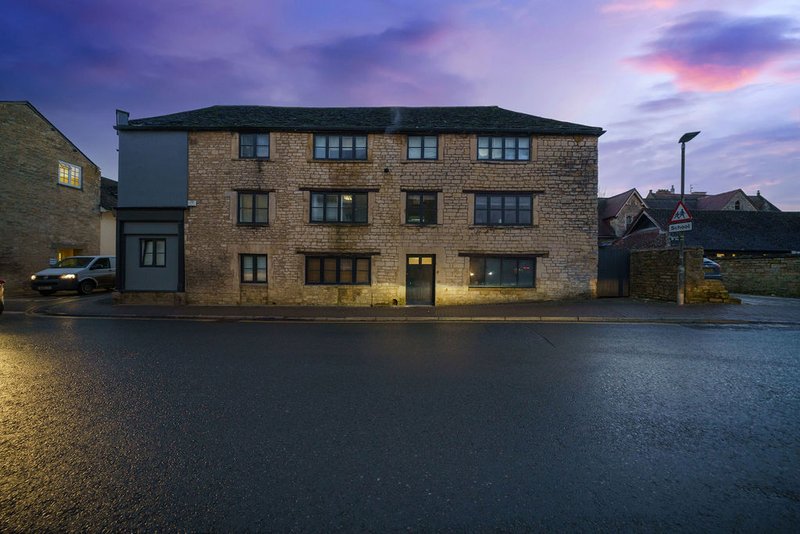 Stone-built residential building exterior at dusk with lit windows and wet pavement