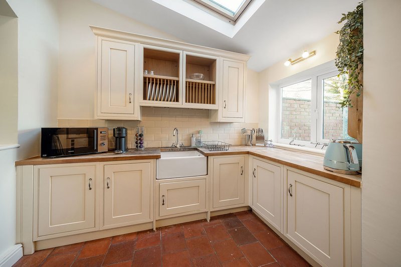 Cream-coloured kitchen with white farmhouse sink, wooden worktops, red terracotta floor and skylight
