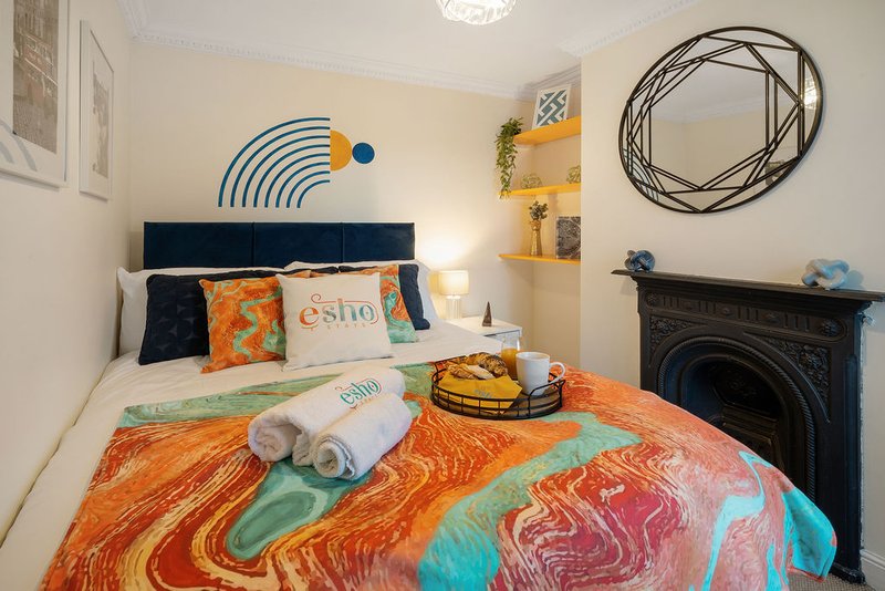 Cozy bedroom with double bed, colorful patterned bedding, navy headboard, wall art and fireplace