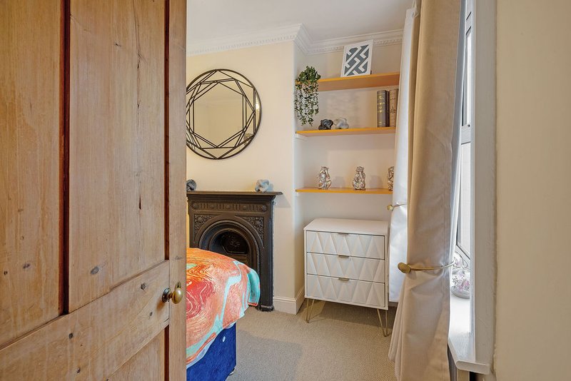 Bedroom with wooden wardrobe, fireplace, decorative wreath, shelving unit and window