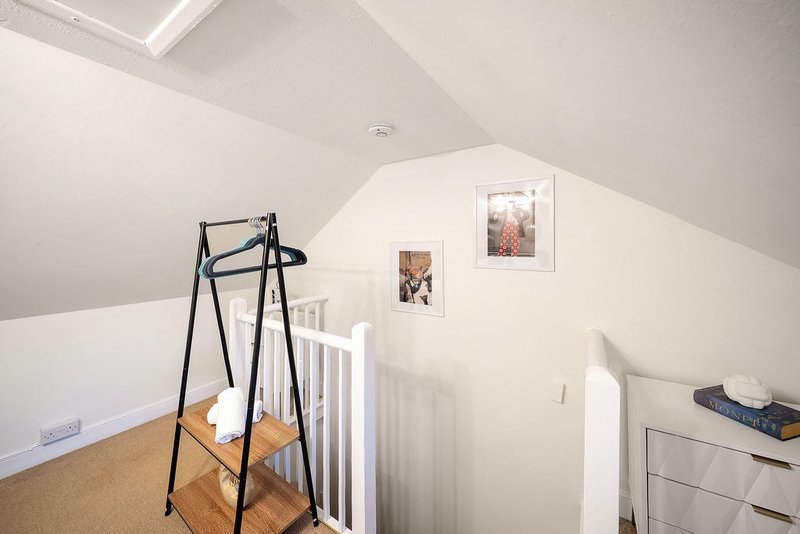 Bright attic bedroom with sloped ceiling, clothes rail, cot, dresser and framed wall art