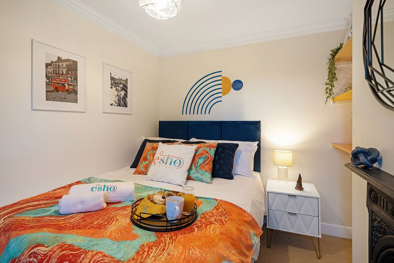 Modern bedroom with double bed, blue headboard, colorful bedding, wall art and bedside lamp