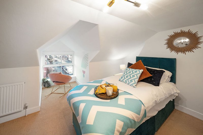 Bright attic bedroom with teal upholstered bed, geometric bedding, decorative cushions and woven wall art