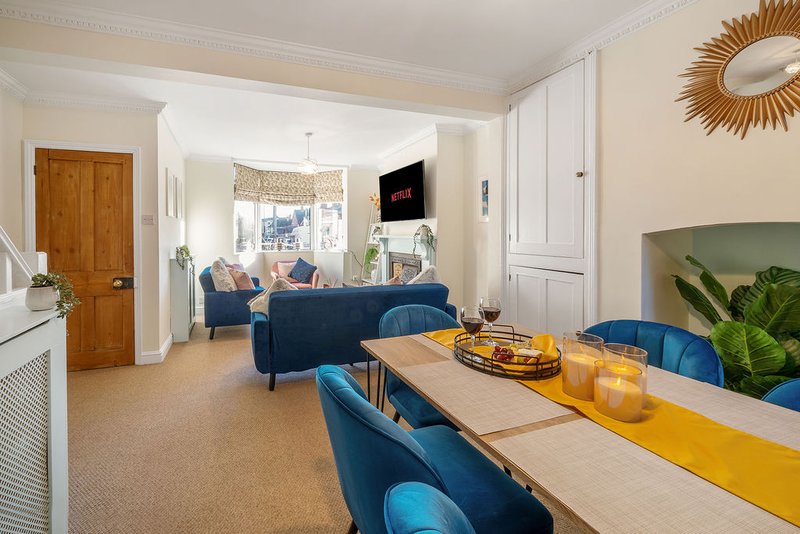 Open-plan living and dining area with blue upholstered furniture, wooden table, and view to lounge