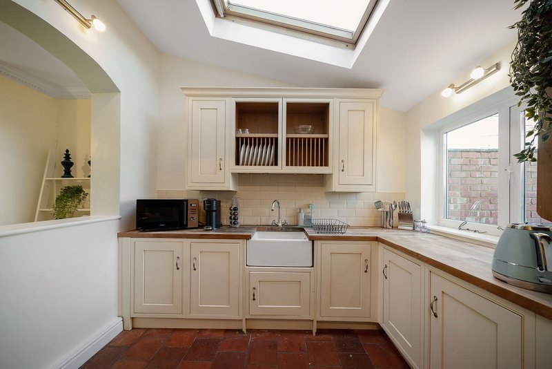 Cream kitchen with cream cabinets, sink, skylight, and brick view through window