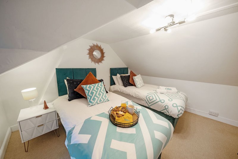 Attic bedroom with double bed, teal headboard, patterned bedding and decorative cushions