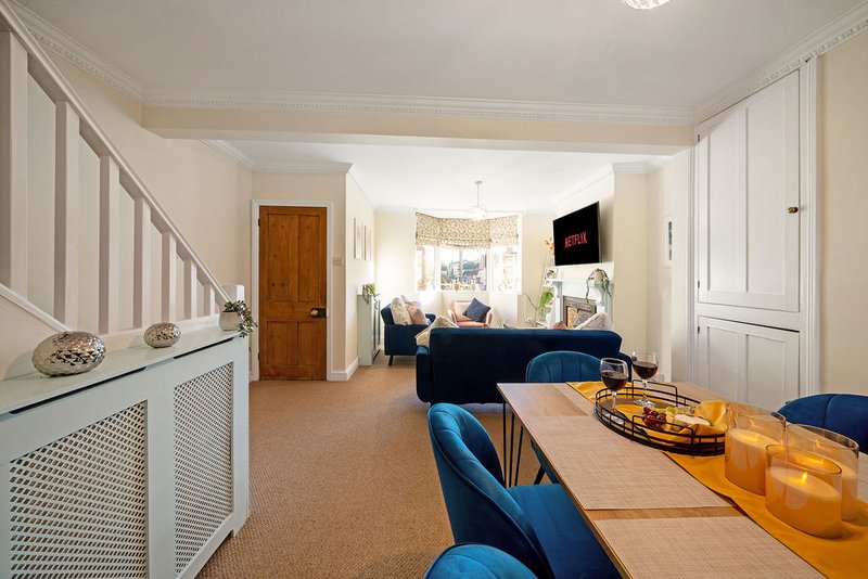 Open-plan living area with dining table, blue chairs, sofa and staircase with white railings