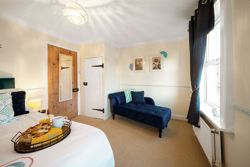 Bright bedroom with double bed, blue velvet sofa, wooden door and window with curtains