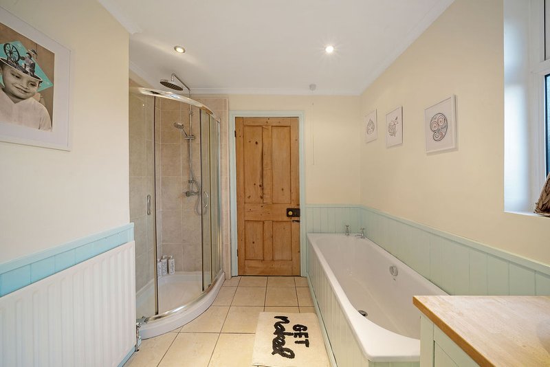 Spacious bathroom with shower enclosure, bathtub, wooden door and cream walls