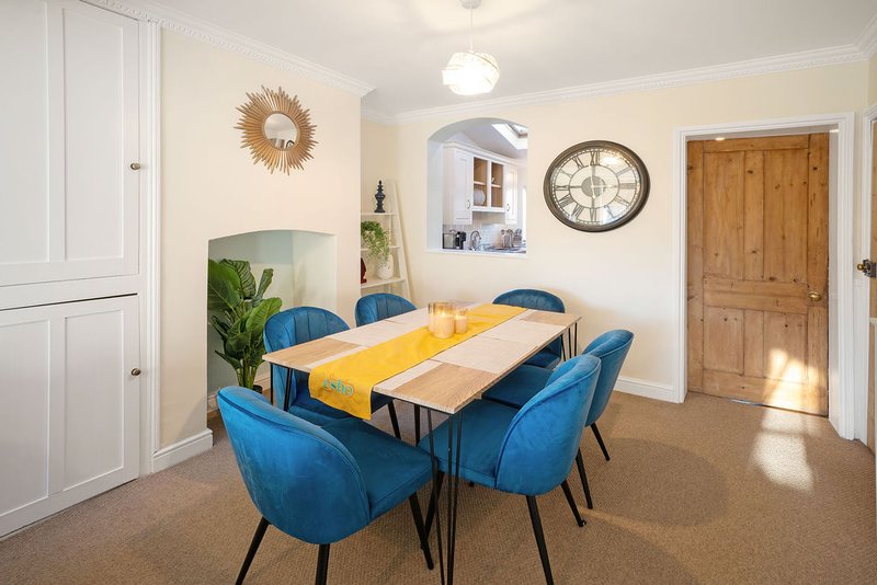 Bright dining room with blue upholstered chairs, yellow table runner, and wall clock decor
