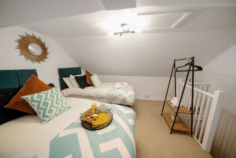 Bright attic bedroom with two beds, teal headboards, decorative pillows and wall art