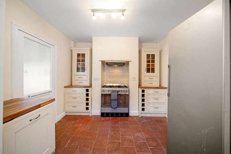 Modern kitchen with cream cabinetry, central range cooker, terracotta tile flooring and overhead lighting