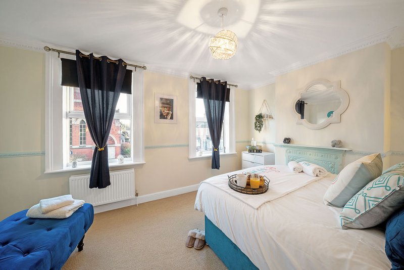 Bright bedroom with twin beds, blue upholstered seating, windows with black curtains and pale walls