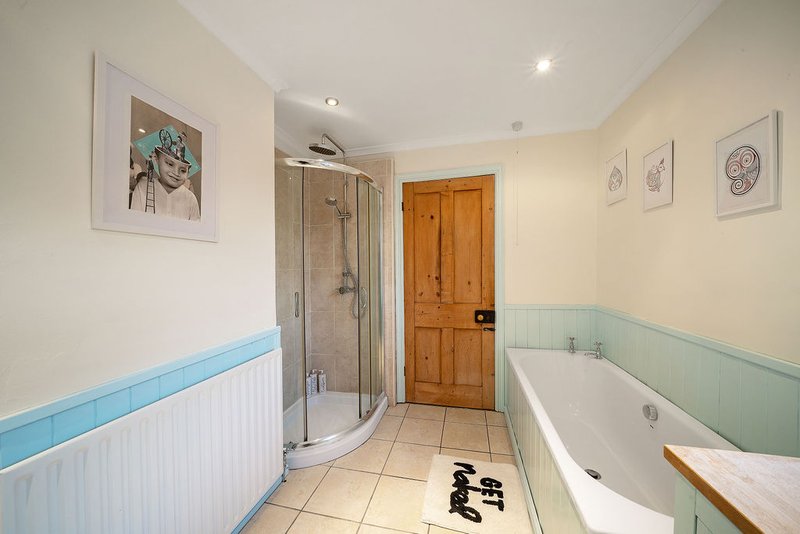 Bathroom with curved shower enclosure, white bathtub, blue and white wall panelling, and framed artwork