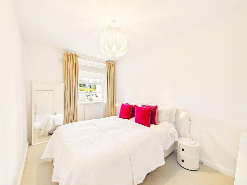 Bright bedroom with white bed, pink cushions, gold curtains and pendant light
