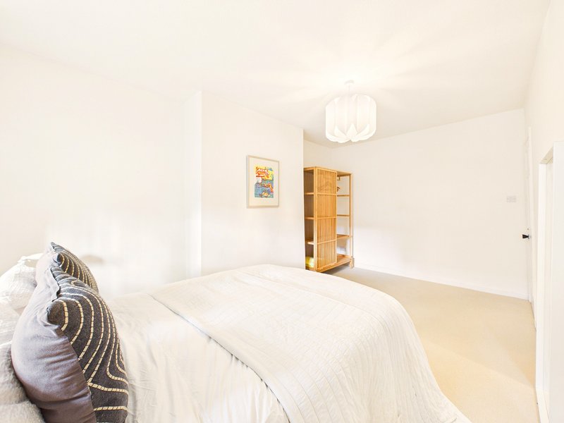 Bright modern bedroom with double bed, decorative pillow, wooden storage unit and ceiling light