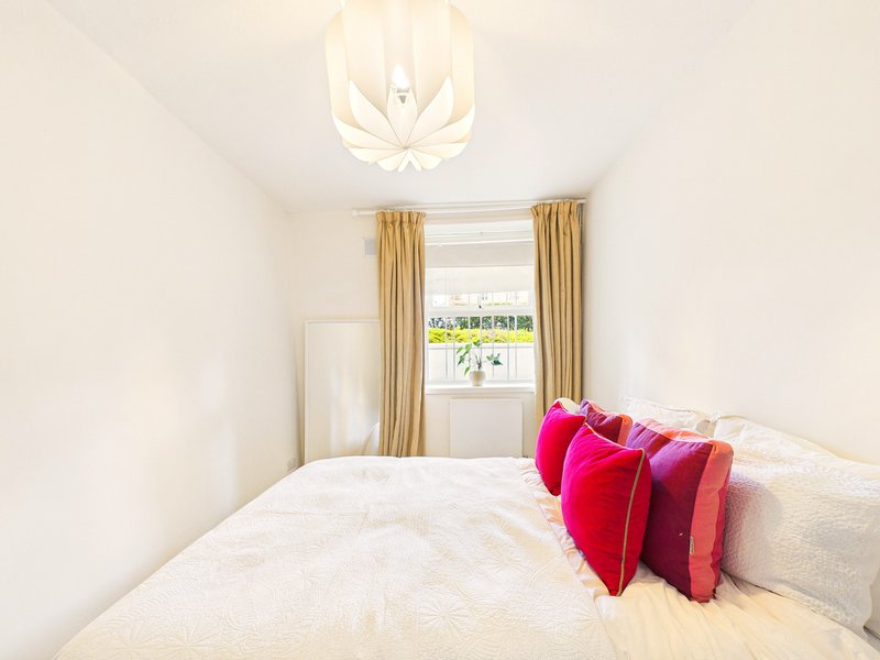 Bright bedroom with double bed, colorful pillows, window with gold curtains and ceiling light
