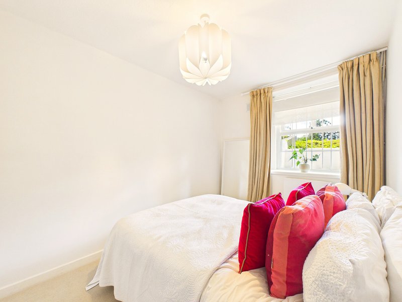 Bright bedroom with double bed, white bedding, pink cushions, modern ceiling light and window with gold curtains