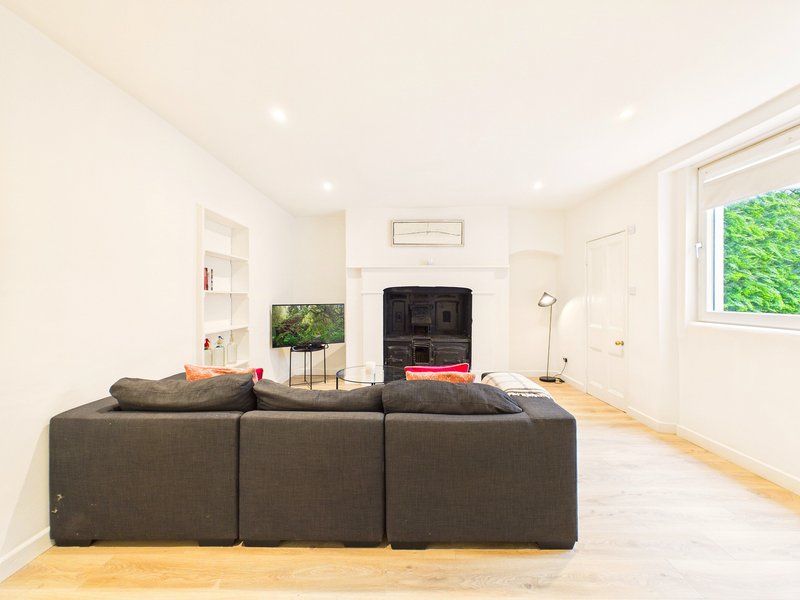 Open-plan living room with grey modular sofa, fireplace, TV, wooden flooring and natural light