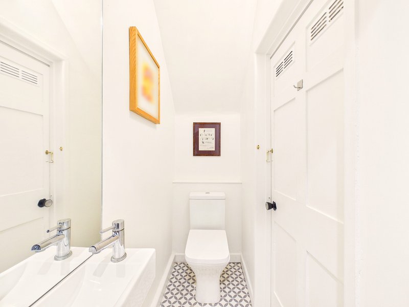 Small bathroom with toilet, white sink, mirror, and decorative wall art