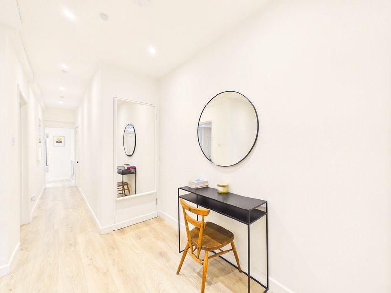 Bright hallway with wooden flooring, console table, yellow chair and round mirror