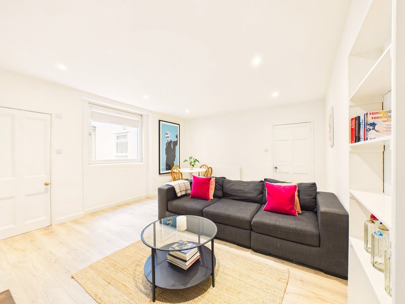 Bright basement living room with dark grey sofa, colorful cushions, round coffee table and wooden flooring
