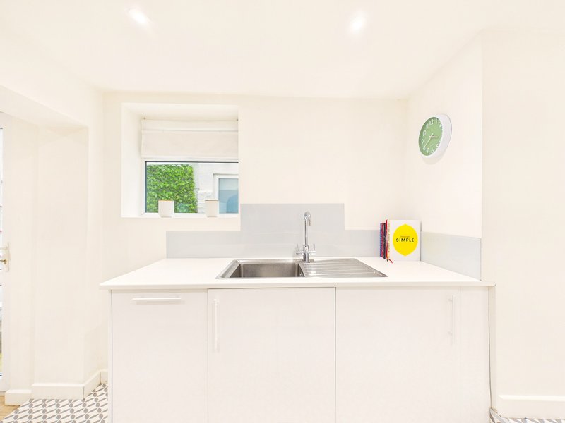 Minimal white kitchen with single sink, cabinets, and window overlooking garden